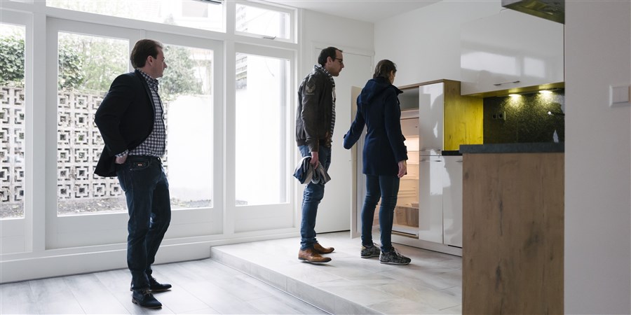 Stel bekijkt keuken bij bezichtiging huis. Makelaar kijkt toe